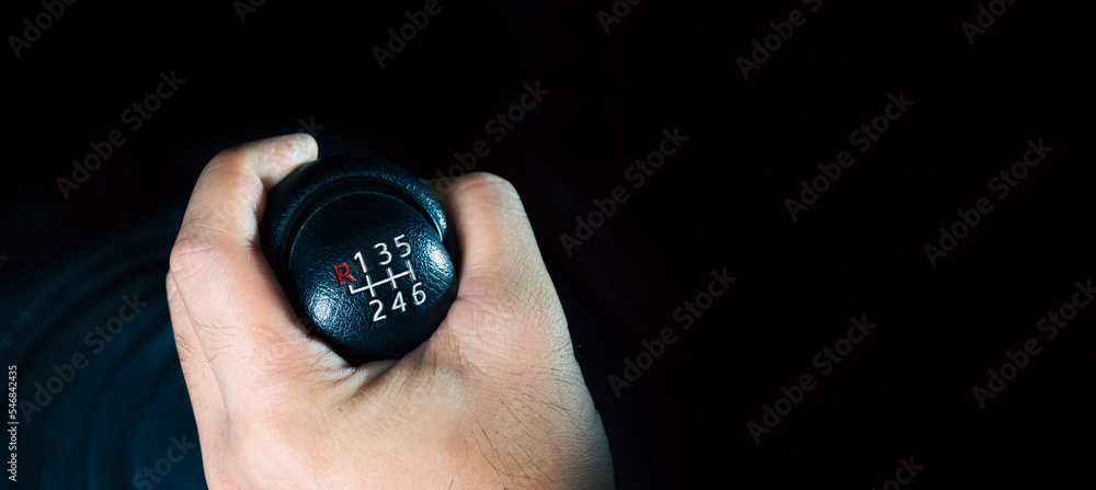 The driver hand is shifting the gears of a 6-speed manual transmission, panoramic banner with copy space on black background