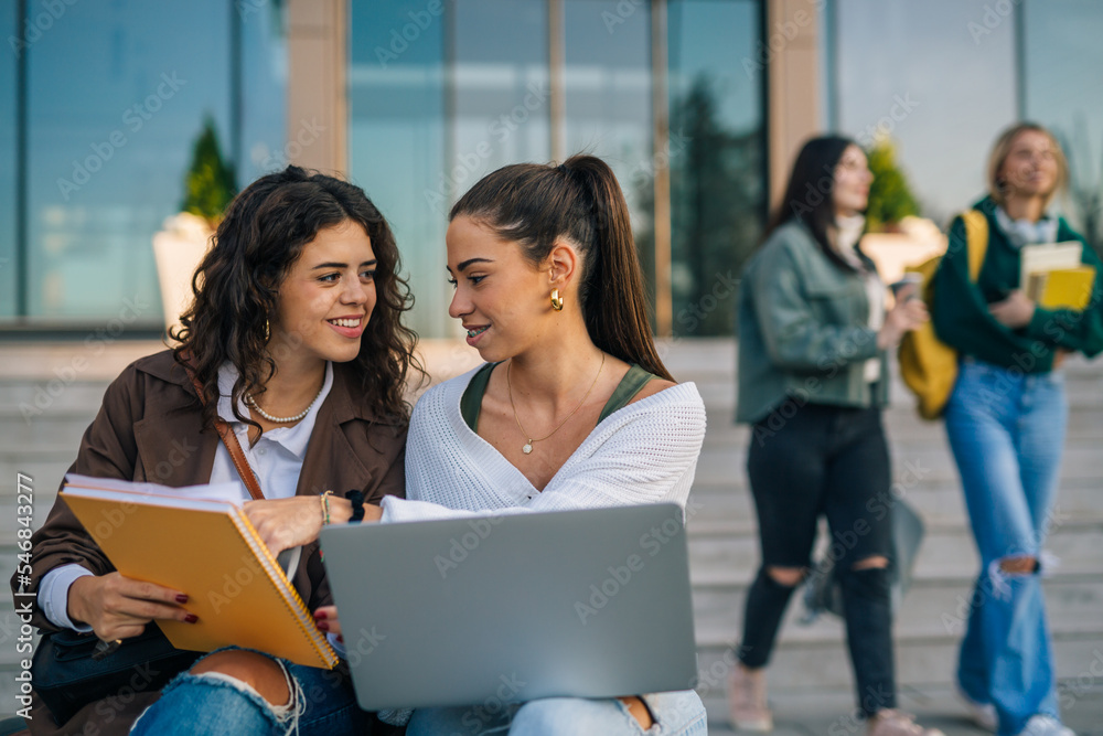 Two girls sit outside and compare notes Two girls sit outside and compare notes