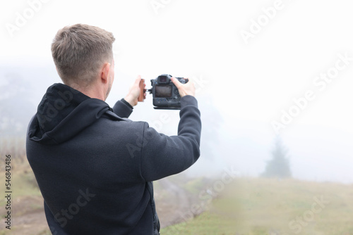 Young male photographer in foggy meadow taking pictures.