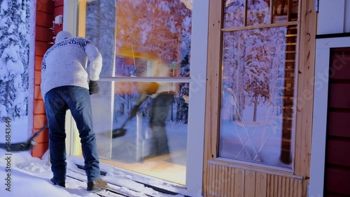 mature man in Scandinavian sweater cleans snow with snowshovel on terrace, snow-covered trees, concept of Severe Weather, Snow Blizzards, weekend in winter forest, active lifestyle, heavy snowfall photo