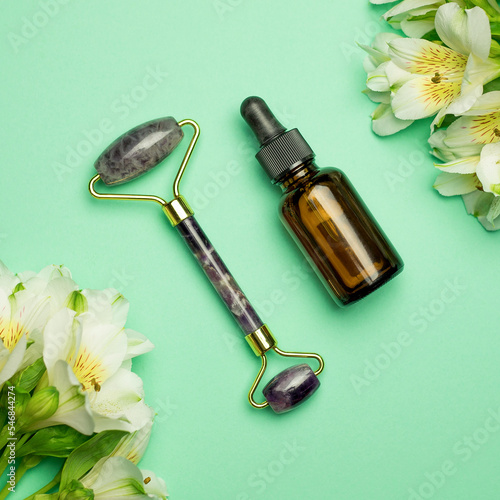 Face roller with beauty serum oil on a green background. Facial massage kit - for lifting massage, made of natural stones.
