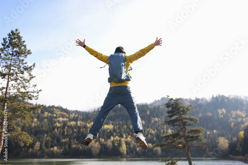 Happy man with open arms jumping, lake and mountains in background.