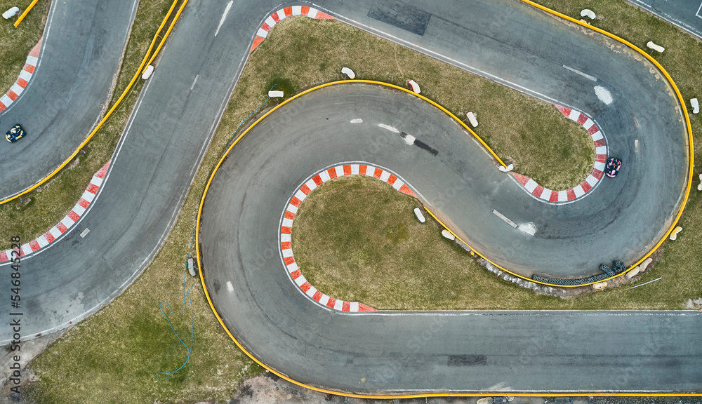 Aerial top view of the go-kart track from the drone. Kart racers drive on the open track. - obrazy, fototapety, plakaty 