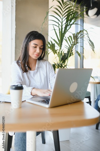 Freelance, business and e-commerce concept. Creative enthusiastic female journalist writing new article, typing on laptop, smiling, write-down project ideas, sit cafe, drink coffee working remote