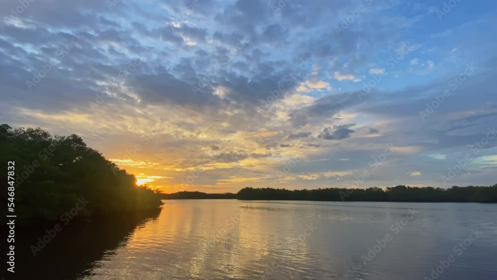Golden Sun Behind Dense Forest Trees With Reflections On Lake Water At Sunset. wide Golden Sun Behind Dense Forest Trees With Reflections On Lake Water At Sunset. wide
