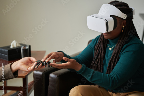 African American girl trying to overcome her phobia of spiders with virtual therapy while visiting psychologist at office photo