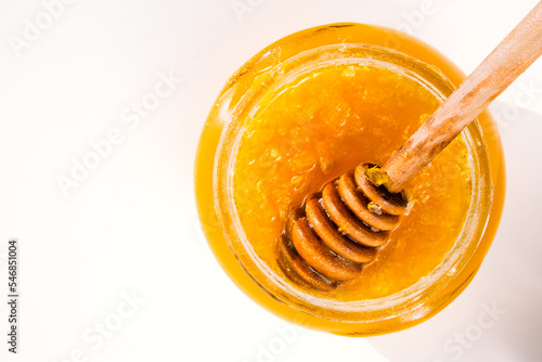 Honey in the glass jar and honey dipper top view on white background. Natural, organic honey close up. Beekeeping concept. Honey products in  sunlight