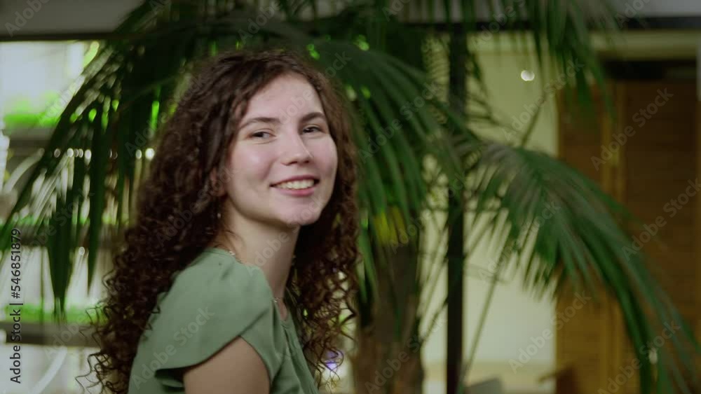 Close-up of a young, very cheerful woman with brown, curly hair, turning to the camera from behind. Portrait of a girl Close-up of a young, very cheerful woman with brown, curly hair, turning to the camera from behind. Portrait of a girl
