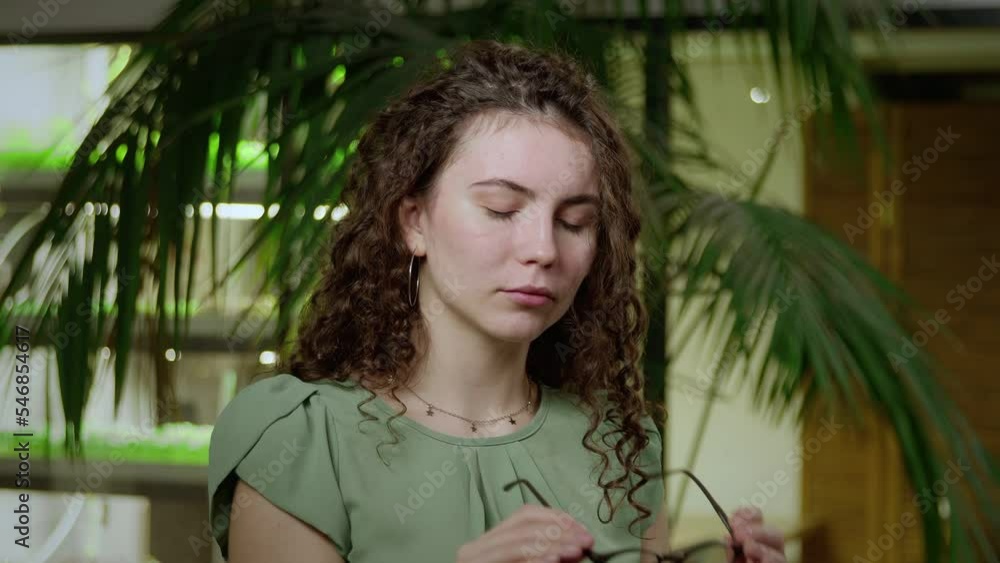 Close-up of a young woman with brown curly hair taking off her glasses and looking at the camera. Portrait of a girl Close-up of a young woman with brown curly hair taking off her glasses and looking at the camera. Portrait of a girl