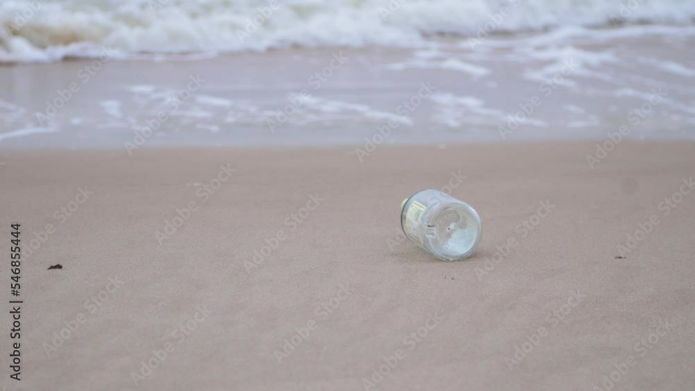 Empty glass bottle on the beach, trash and waste litter on an empty Baltic sea white sand beach, environmental pollution problem, overcast day, medium shot Empty glass bottle on the beach, trash and waste litter on an empty Baltic sea white sand beach, environmental pollution problem, overcast day, medium shot