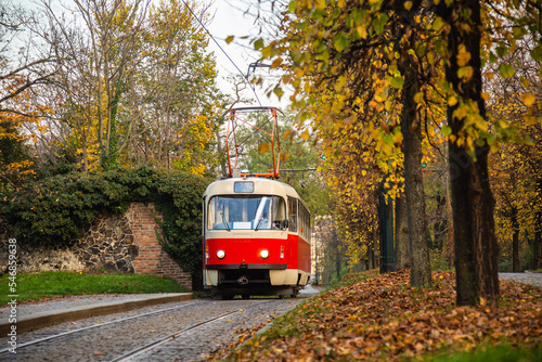 Old vintage tourist tram comes through the alley of a Prague city in an autumn day. Electric transport connection. Prague tram network is third largest in a world. Retro historic electro transport