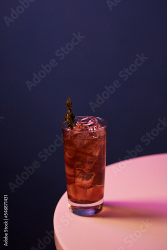 red cocktail with alcohol and ice and rosemary in a highball glass, on a white table