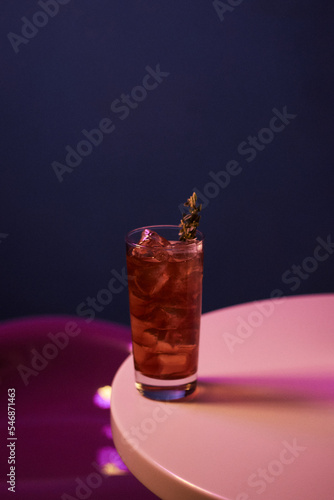 red cocktail with alcohol and ice and rosemary in a highball glass, on a white table