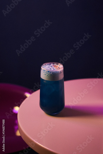 
blue cocktail with alcohol and foam in a highball glass, on a white table