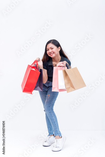 An elated asian woman holding shopping bags on both hands after going on a shopping spree. Isolated on a white background. Retail and sale concepts.