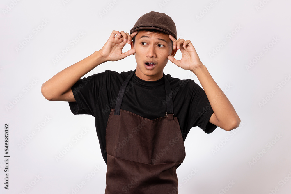 Handsome barista asian man wearing brown apron and black t-shirt isolated over white background shocked with surprise and amazed expression