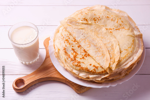 Stack of thin pancakes on plate and glass of milk