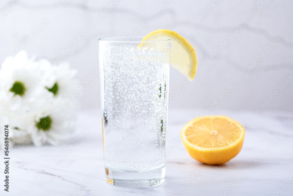 Glass of water with a slice of lemon on a background of blurred chrysanthemum flowers. Glass of water with a slice of lemon on a background of blurred chrysanthemum flowers.