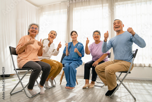 Asian group of elderly people who are smiling and holding up their thumbs in a circle with a doctor during Self help therapy meeting