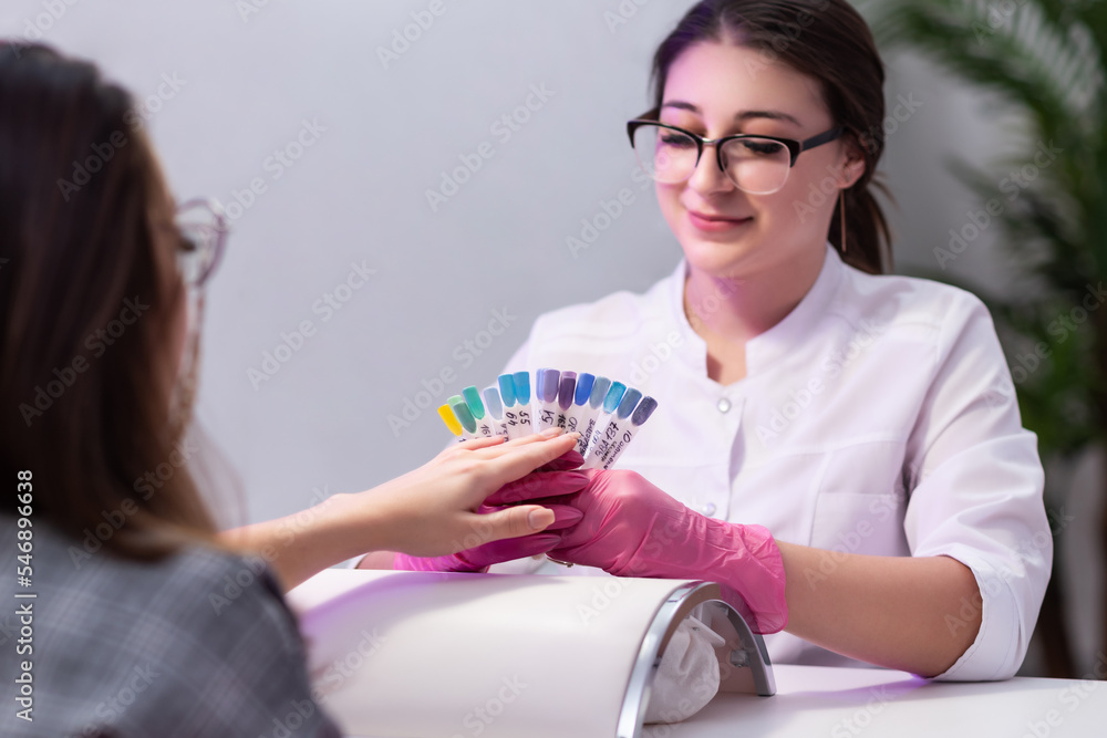 Manicurist in pink gloves demonstrates a palette of nail polish samples to a client. The girl does a manicure in a beauty salon. Nail care. Cosmetic procedures Manicurist in pink gloves demonstrates a palette of nail polish samples to a client. The girl does a manicure in a beauty salon. Nail care. Cosmetic procedures