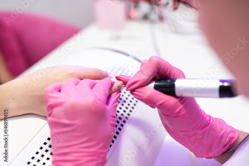 Close-up of a girl doing a manicure in a beauty salon. Nail care. Manicurist in pink gloves removes gel polish from nails with a fresco. Hardware manicure revealed. Cosmetic procedure