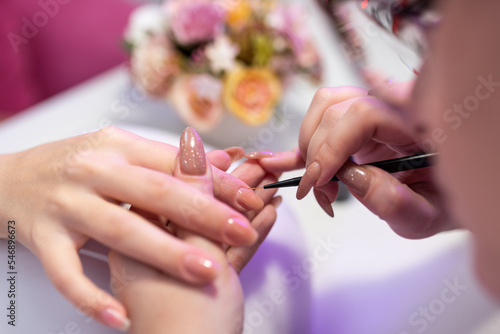 Close-up of a girl doing a manicure in a beauty salon. Nail care. Manicurist corrects the applied varnish with a thin brush. Cosmetic procedure