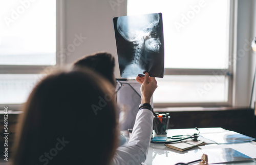 Faceless doctor examining cervical spine x ray image during consultation with patient photo