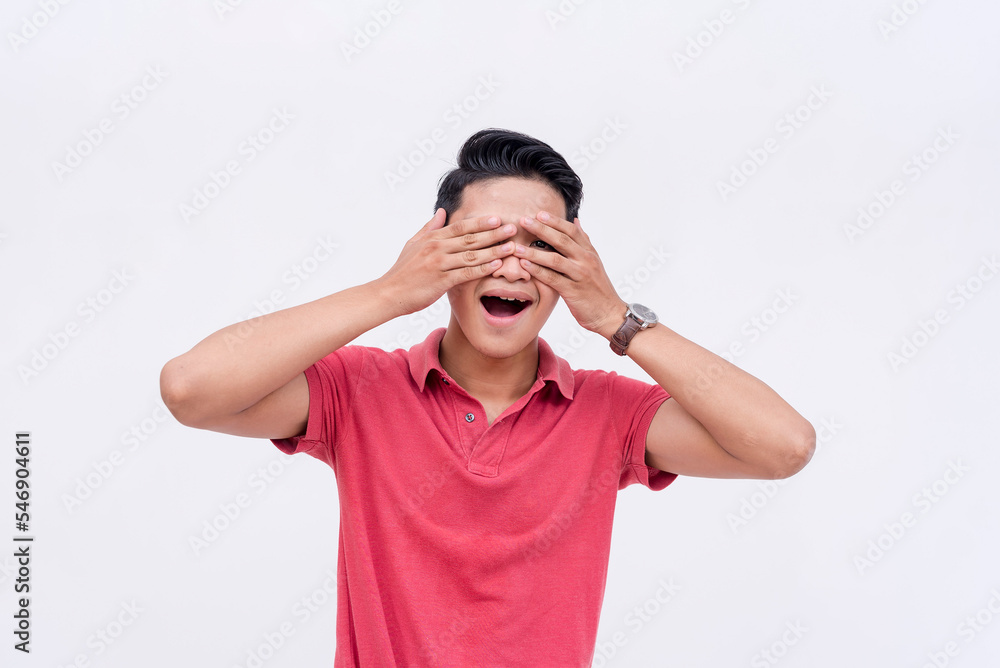 A young asian man covers his face but peeping with one eye. Too impatient to wait for the surprise. Isolated on a white background. Spoiler alert concept. A young asian man covers his face but peeping with one eye. Too impatient to wait for the surprise. Isolated on a white background. Spoiler alert concept.