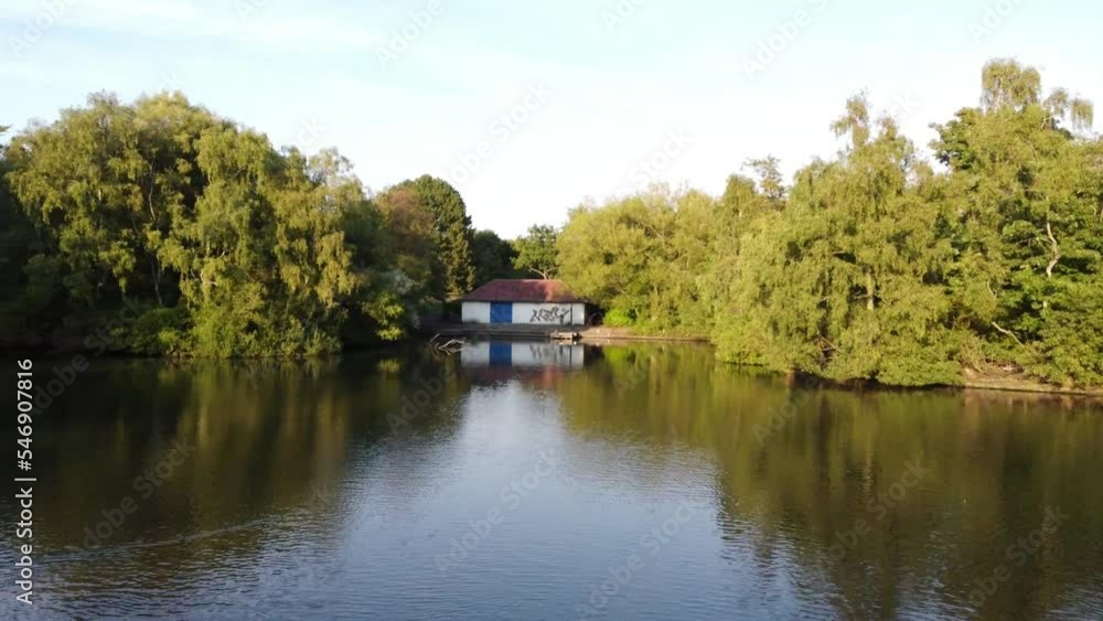 Low ariel drone view parkland lake wading birds. Landscape has wooded forestry area trees bushes stone building shed. Beautiful scenic sunny day sunshine on calm water blue sky above captured in 4k. Low ariel drone view parkland lake wading birds. Landscape has wooded forestry area trees bushes stone building shed. Beautiful scenic sunny day sunshine on calm water blue sky above captured in 4k.