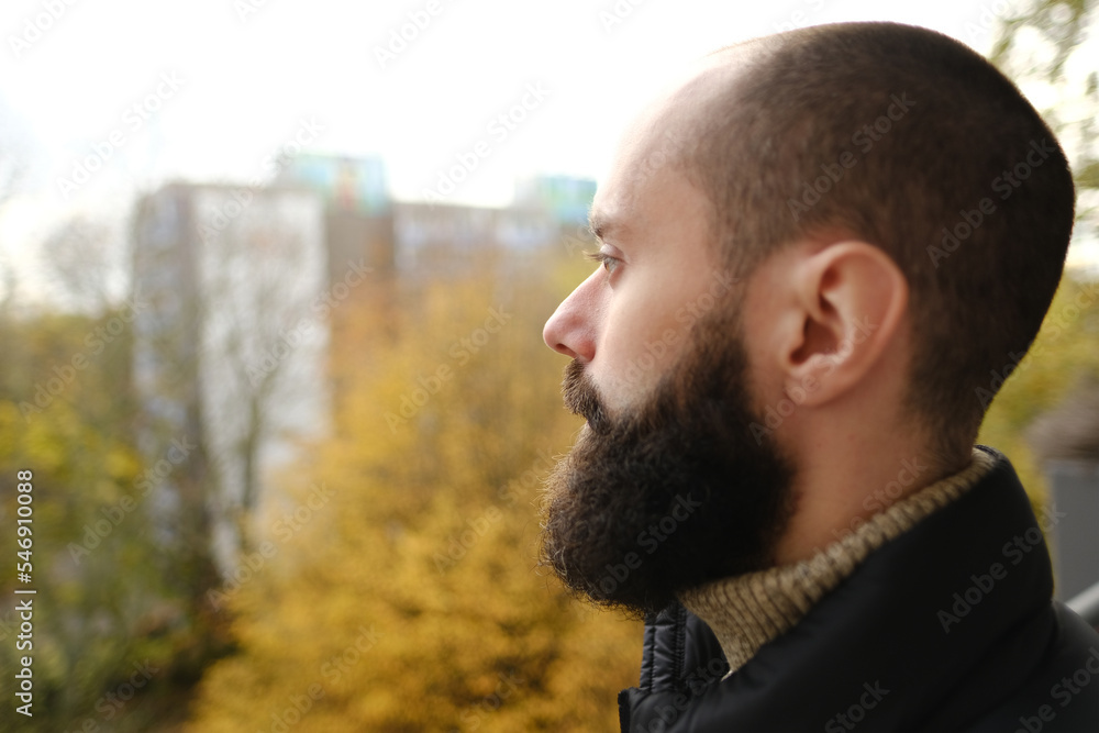 young pensive bearded and mustachioed man, satisfied guy with 30 years in black jacket stands on balcony, seriously looks away, concept of human health, reflections on meaning of life young pensive bearded and mustachioed man, satisfied guy with 30 years in black jacket stands on balcony, seriously looks away, concept of human health, reflections on meaning of life