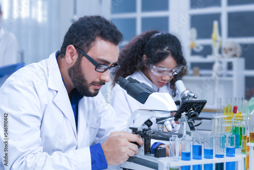 A team of male and female scientists or researchers wearing white coats and a microscope congratulate 'the cows on target'.