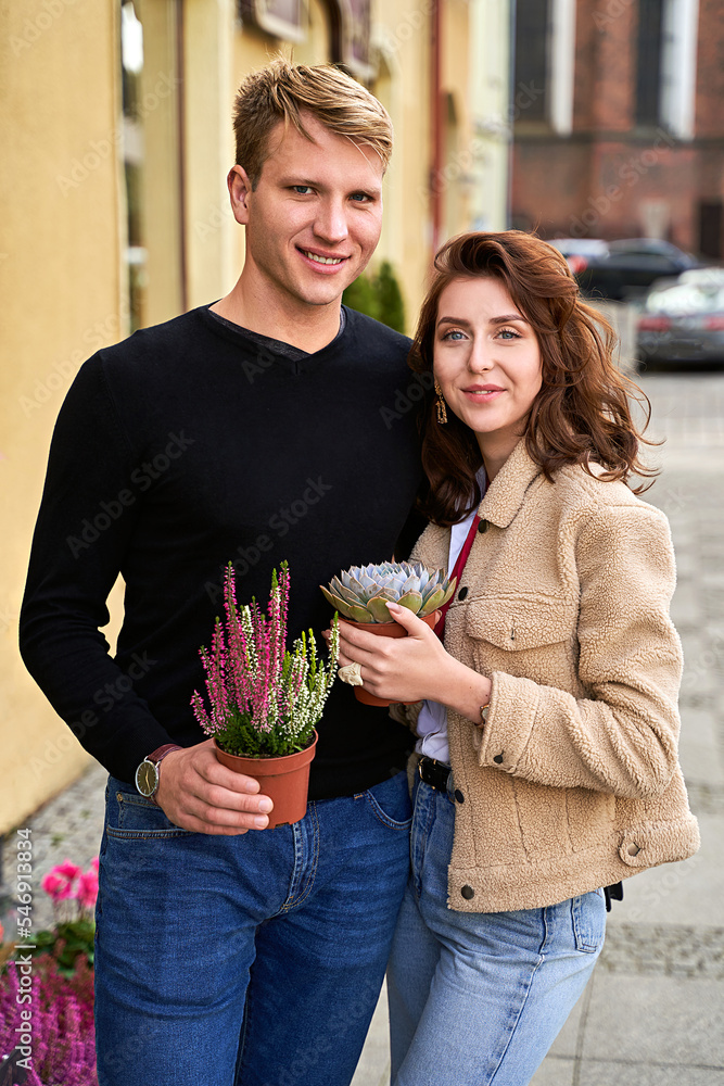 Man and woman holding a purple sempervivum succulent plant and blooming violet heather plant
