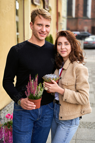 Man and woman holding a purple sempervivum succulent plant and blooming violet heather plant