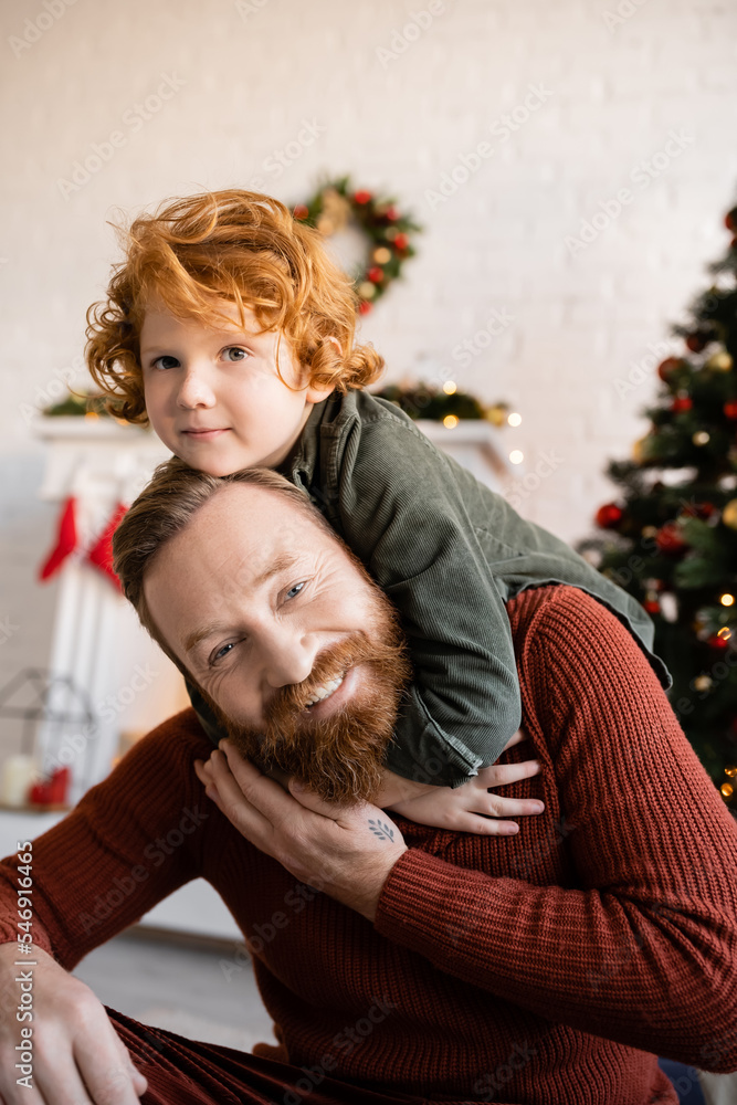 cheerful bearded man playing with redhead son during Christmas celebration cheerful bearded man playing with redhead son during Christmas celebration