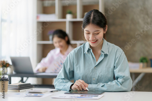 Beautiful young Asian business woman using tablet to work smiling and enjoying her job.