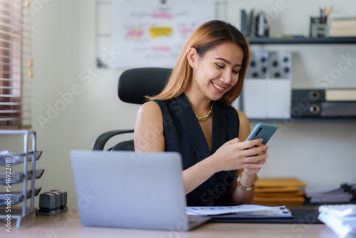 Happy Asian businesswoman working with a smile and using her smartphone for business communication respond to chats and talk to various LINE applications in the office.