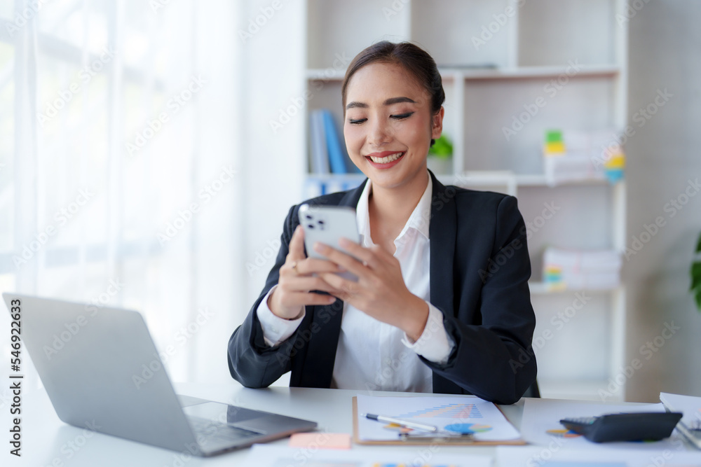 Happy Asian businesswoman working with a smile and using her smartphone for business communication respond to chats and talk to various LINE applications in the office. Happy Asian businesswoman working with a smile and using her smartphone for business communication respond to chats and talk to various LINE applications in the office.