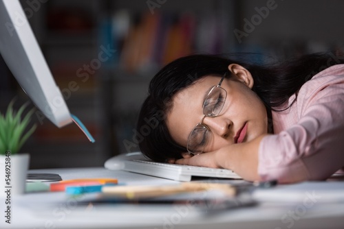 A woman is sleeping, having head on a laptop.