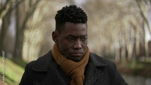 Contemplative man walking outside at park during winter wearing coat and scarf