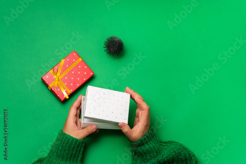 An ajar gift box in female hands over the table, gift boxes lie nearby, a Christmas tree, green background