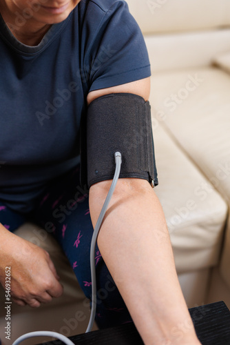 Senior woman checking blood pressure level at home  older female suffering from high blood pressure sitting at a couch and using a pulsometer  tonometer