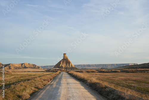 Long gravel road heading to the famous Bardenas natural monument under a clear blue cloudy sky. Semi-desert landscape in the north of Spain, Navarra.