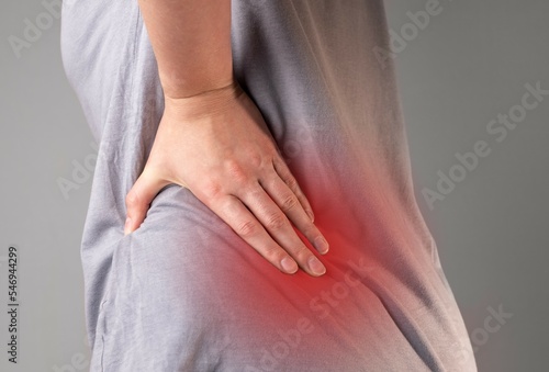 Backache concept. Hand holding painful aching lowe back, loin, highlighted red spot