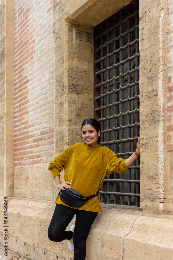 Young woman smiling and wearing yellow sweater posing in front of an old building