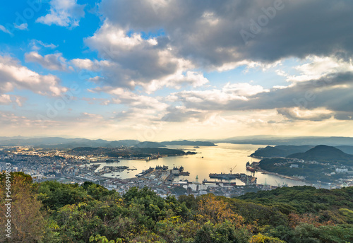 kyushu, japan - december 09 2021: Bird's-eye view from the deck of the Yumiharidake Observation Point overlooking the Sasebo shipyard with the Kujukushima islands off coasts in background at sunset. © kuremo