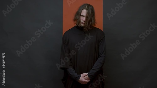 Horizontal medium studio portrait footage of scary young Caucasian man with messy hairstyle wearing black outfit standing against black and brown backgroundHorizontal medium studio portrait footage of photo