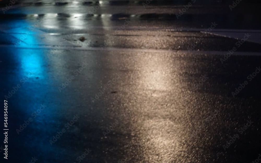 Nasse asphaltierte graue Straße mit blauer und weißerLichtspiegelung in Stadt bei Regen in der Nacht im Herbst Nasse asphaltierte graue Straße mit blauer und weißerLichtspiegelung in Stadt bei Regen in der Nacht im Herbst