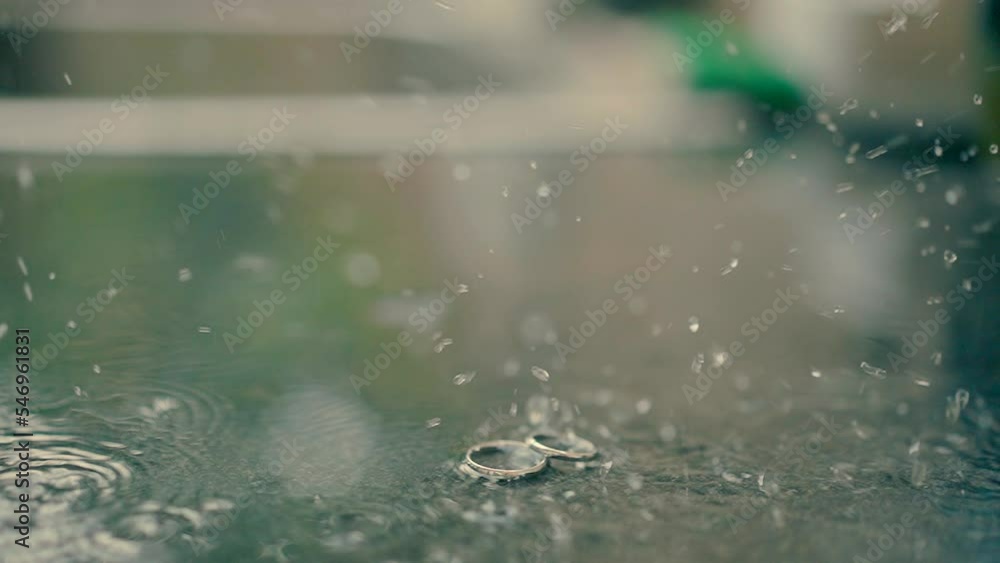 Wedding rings in a puddle and rain pouring down on them in the afternoon. A rainy wedding day. Slow motion video shooting of two rings outside. Close up video. slow motion Wedding rings in a puddle and rain pouring down on them in the afternoon. A rainy wedding day. Slow motion video shooting of two rings outside. Close up video. slow motion
