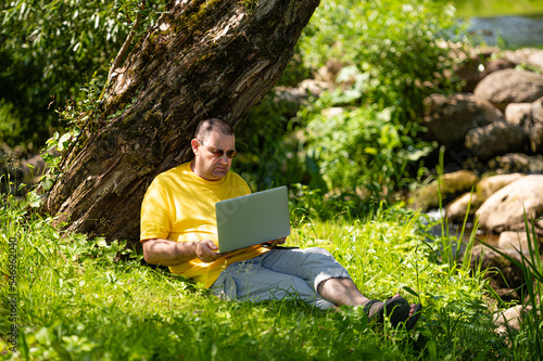 man with laptop and smartphone working outside in the meadow by the river, outdoor office concept