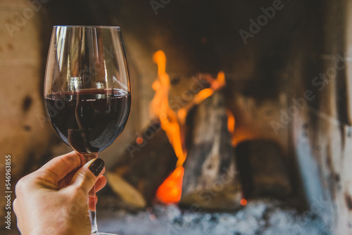 Mão segurando taça de vinho tinto em lareira no inverno